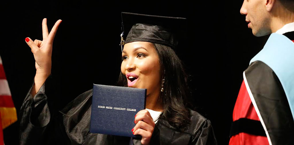 NECC gives a peace sign with her fingers on stage at commencement