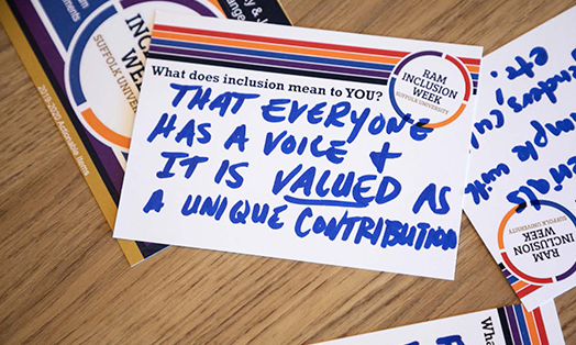 Photograph of cards completed by Ram Inclusion Week participants. The card in focus features a handwritten response to the question 'What does inclusion mean to you?' and reads 'That everyone has a voice and it is VALUED as a unique contribution'.