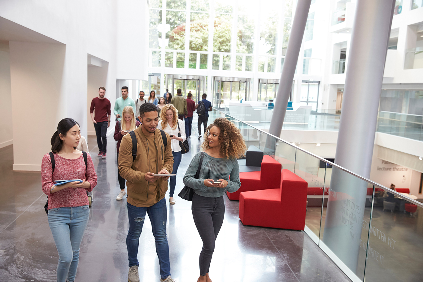 Students holding tablets and phone talk in university lobby