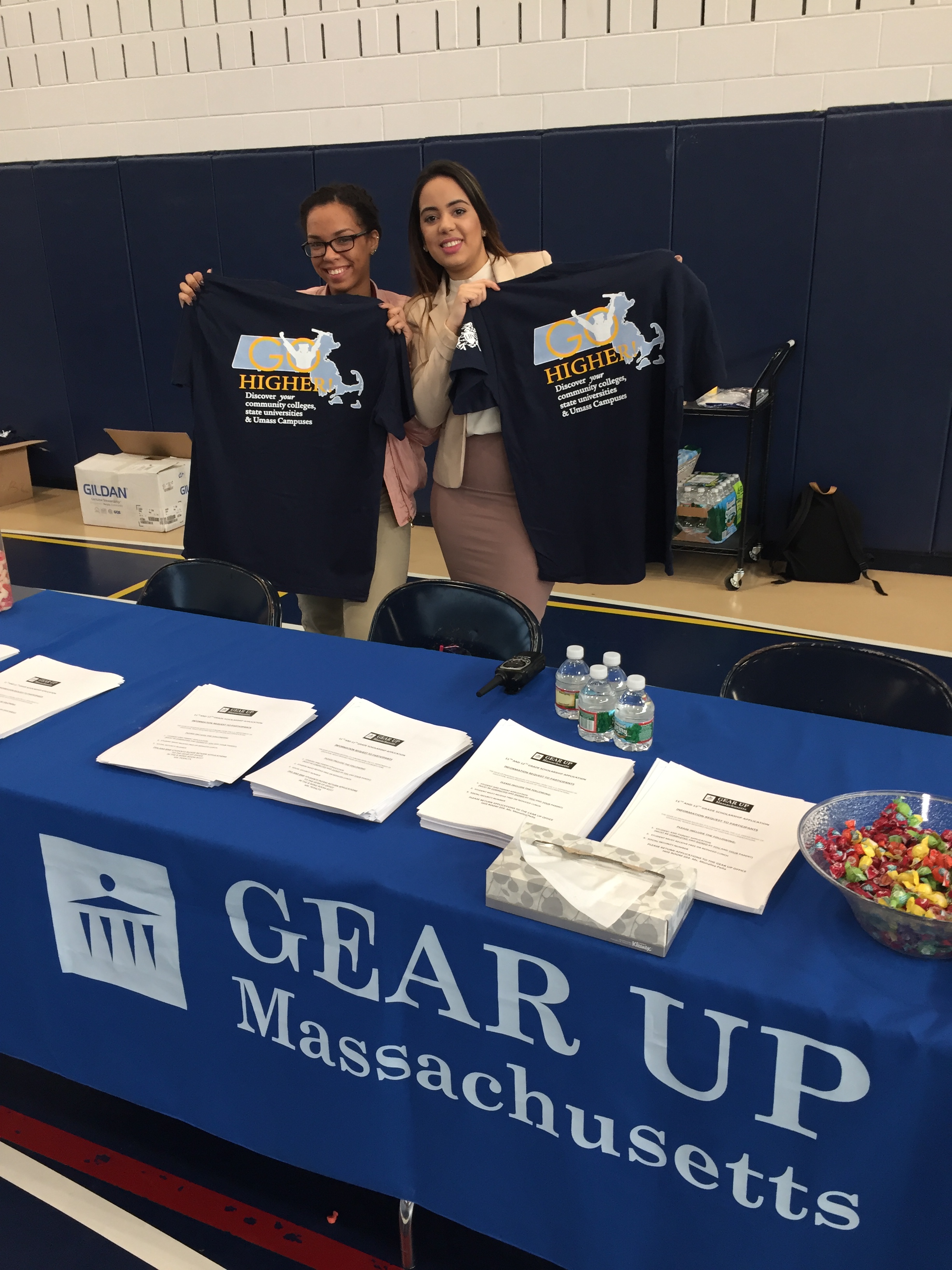 Two people hold up 'Go Higher' t-shirts at the GEAR UP table