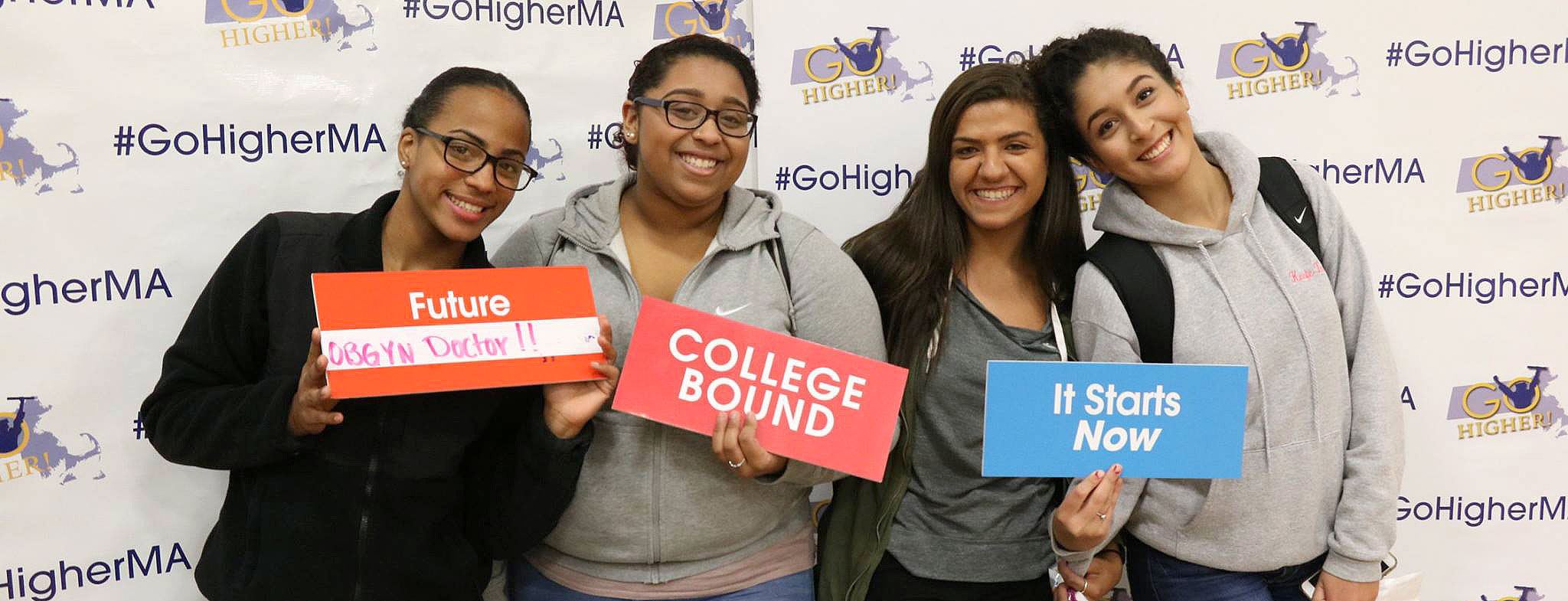 Students pose in the #GoHigherMA photo booth with signs that read 'Future OGBYN doctor,' 'COLLEGE BOUND,' and 'It Starts Now.'